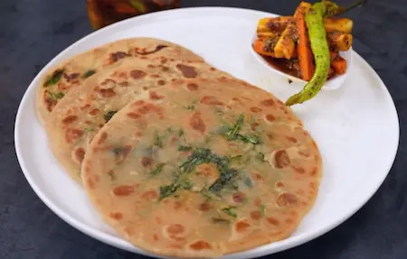 Golden brown spinach paratha being cooked on tawa and served with achar