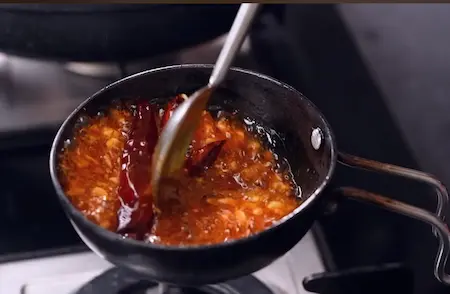 Preparing tadka with cumin seeds, garlic, and red chilies