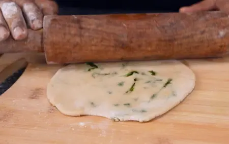 Wheat dough ball being stuffed with spinach masala and rolled into paratha