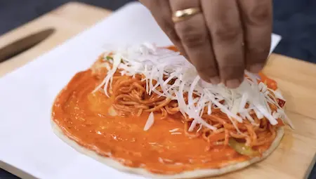 Street style frankie being assembled with noodles, cabbage, onion and sauces on a flatbread