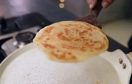 Cooking shaped parottas on hot tawa until golden and crispy