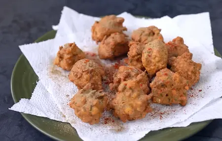 Draining Crispy Corn Pakoda on paper towel and sprinkling chaat masala for flavour