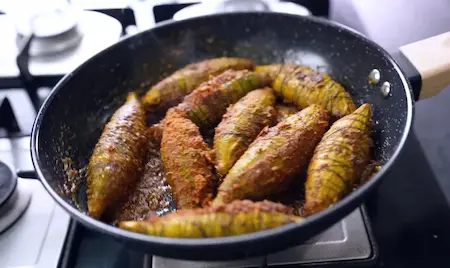 Stuffed karelas being shallow fried with fennel seeds in mustard oil for Soya Kheema Karela Recipe