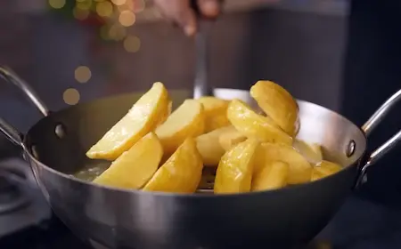 Shallow frying coated potato wedges until crispy golden for Goan Chilli Potato
