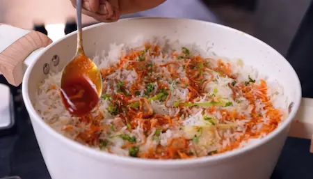 Adding final toppings to the biryani for flavor.
