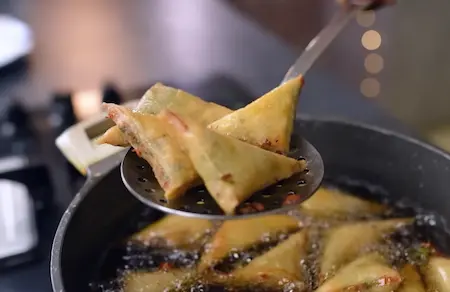 Deep frying golden crispy Cheesy Corn Palak Samosas in hot oil