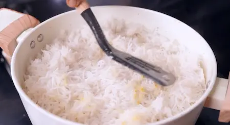 Adding the partially cooked rice to the biryani.