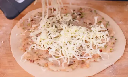 Step 3: Adding potato stuffing and grated cheese to rolled dough for paratha