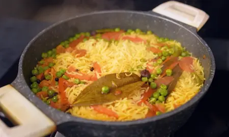 Spiced rice cooking with peas and fried mangodi in a covered pan
