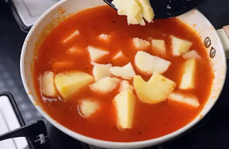 Cubed boiled potatoes cooking in tomato and black pepper gravy for Aloo Kali Mirch