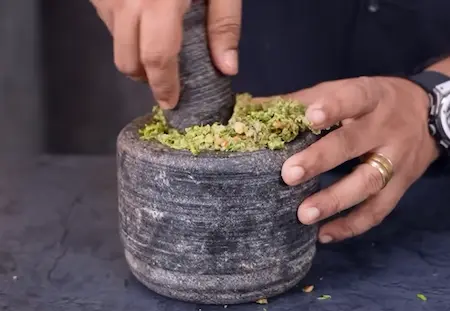 Green chili garlic thecha being prepared with peanuts and spices