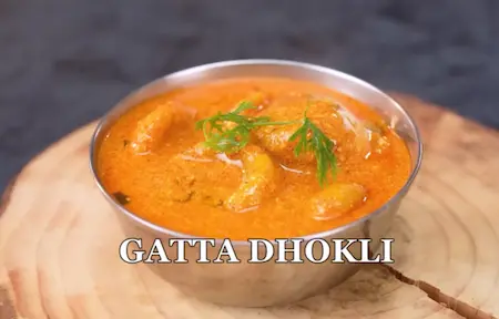 Flattened besan dumplings cooking in spiced yogurt gravy