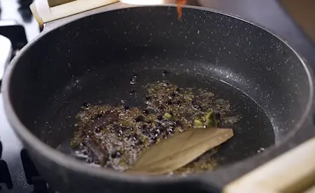 Heating oil with shahi jeera, cloves, cinnamon, and other whole spices in a pan for Masoor Dal Pulao